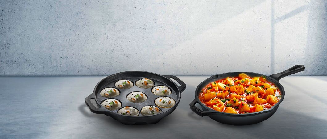 Cast iron cookware set featuring an appam pan with cooked appams and a skillet filled with curry, placed on a kitchen countertop