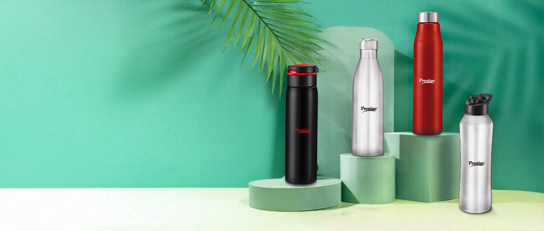 Four Prestige stainless steel water bottles in black, silver, and red colors displayed on green podiums against a tropical-themed green background.