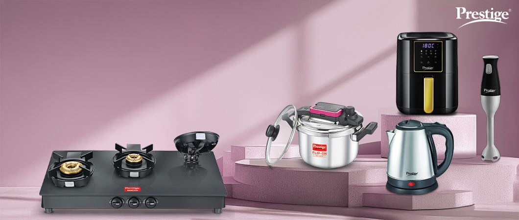 Prestige kitchen appliances including black gas stove, silver pressure cooker, black air fryer, electric kettle, and hand blender on a pink background.
